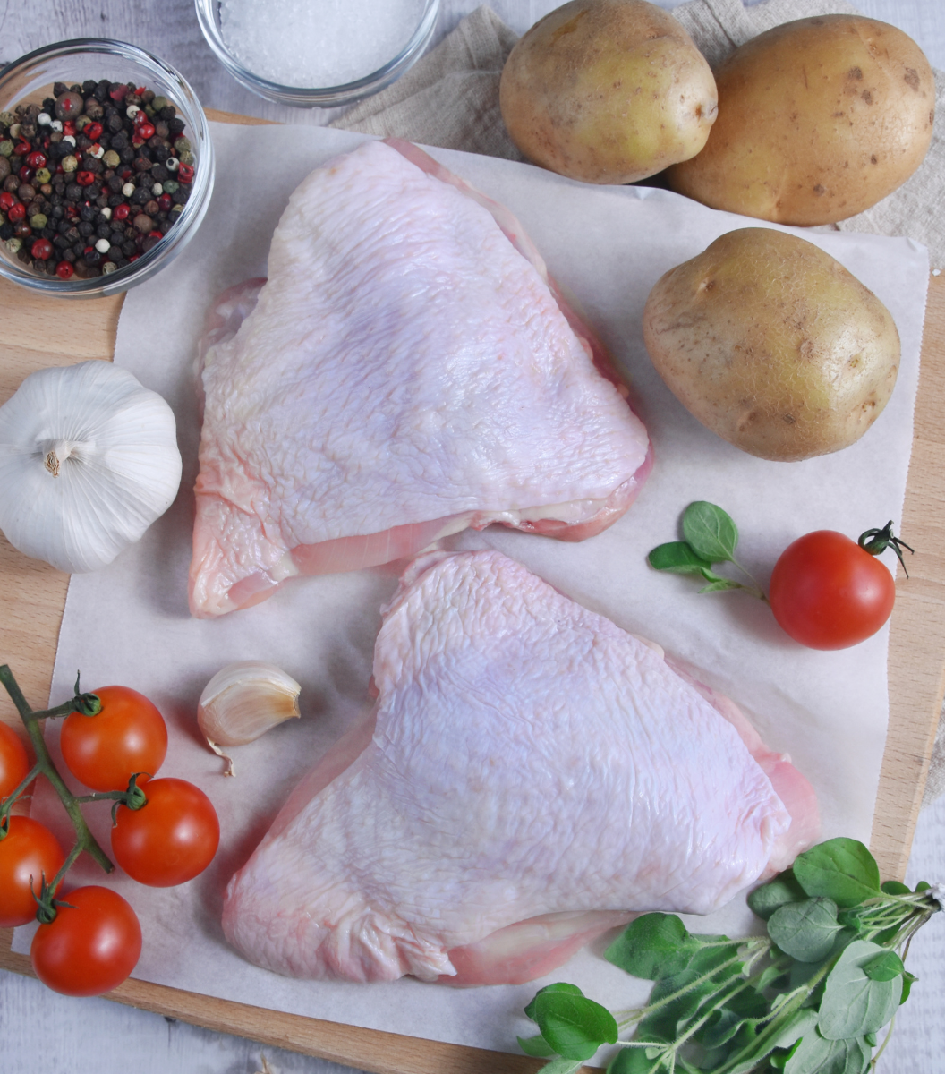 2 Fresh raw chicken thigh bone-in with potatoes, cherry tomatos and garlic on wooden board.